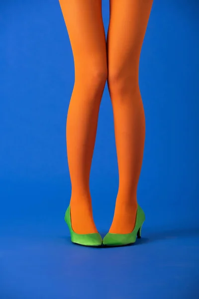 Vista cortada da mulher em meias laranja brilhante e sapatos verdes posando em azul — Fotografia de Stock