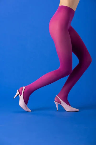 Vista ritagliata del modello in collant viola brillante e scarpe in piedi su blu — Foto stock
