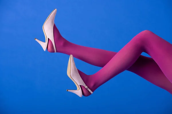 Обрезанный вид модели в ярко-фиолетовых колготках и каблуках, позирующих на синем — стоковое фото