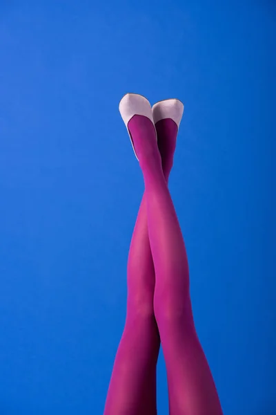 Vue recadrée du modèle en collants violets et chaussures aux jambes croisées sur bleu — Photo de stock