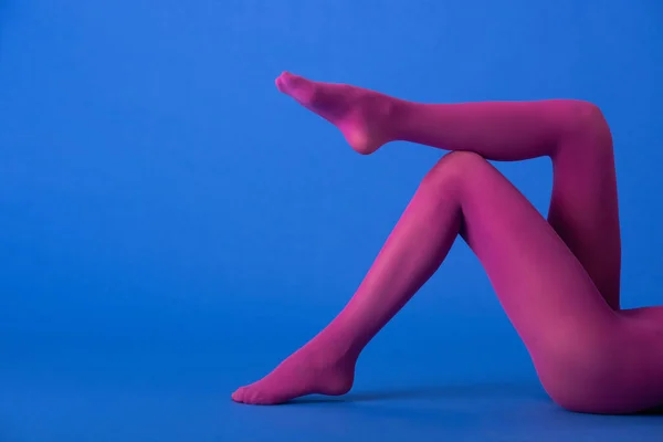 Cropped view of woman in bright purple tights sitting on blue — Stock Photo
