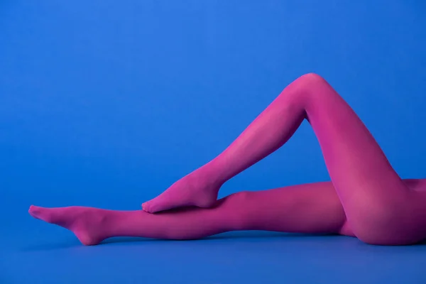 Recortado vista de la mujer en púrpura medias acostado en azul - foto de stock