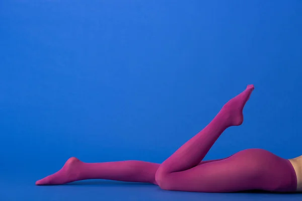 Обрезанный вид модели в модных фиолетовых колготках, лежащих на голубом — стоковое фото
