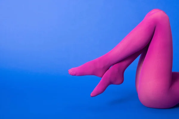 Vue recadrée du modèle en collants violets avec jambes croisées posant sur bleu — Photo de stock