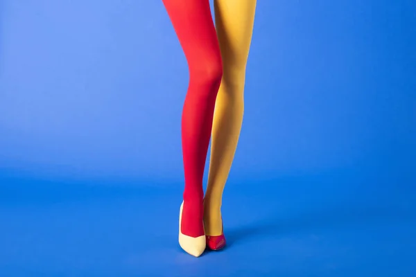 Vista recortada del modelo en medias y zapatos amarillos y rojos de pie sobre azul - foto de stock