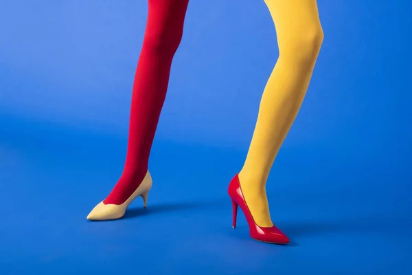 Vista cortada da mulher em meias amarelas e vermelhas e saltos posando em azul — Fotografia de Stock