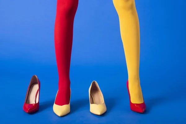 Vista cortada de modelo elegante em meias amarelas e vermelhas e sapatos posando em azul — Fotografia de Stock