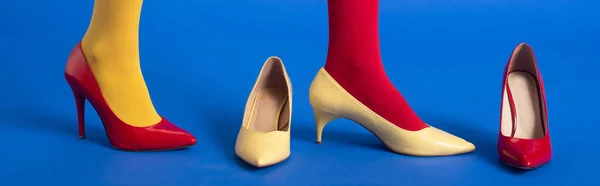 Plano panorámico de mujer en medias y zapatos rojos y amarillos posando sobre azul - foto de stock