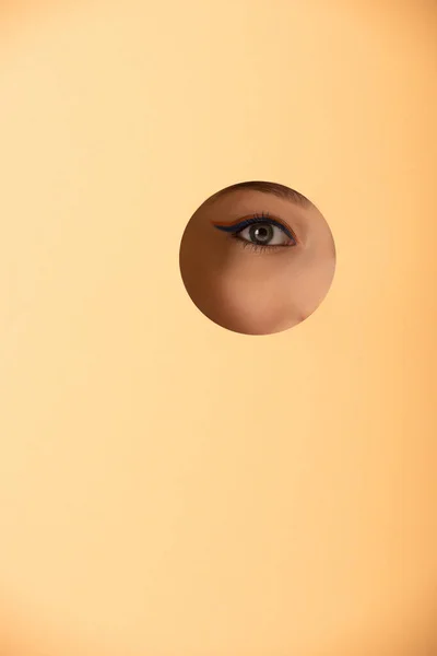 Cropped view of woman looking at camera through hole on pastel orange — Stock Photo