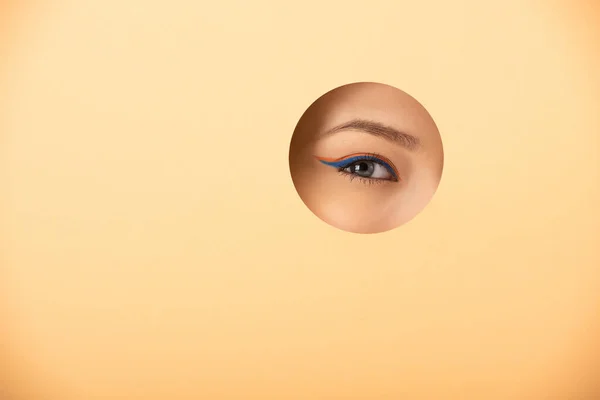 Vista ritagliata della donna guardando la fotocamera attraverso il foro su arancione — Foto stock