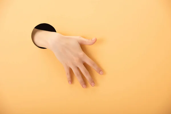 Обрезанный вид дыры с рукой женщины на оранжевом — стоковое фото