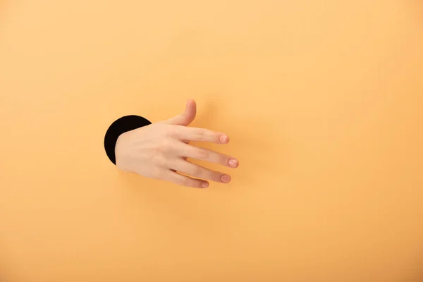 Обрезанный вид дыры с рукой женщины, жестикулирующей на апельсине — стоковое фото