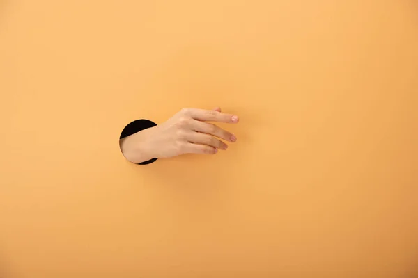 Vista recortada del agujero con la mano de la mujer haciendo un gesto en naranja - foto de stock