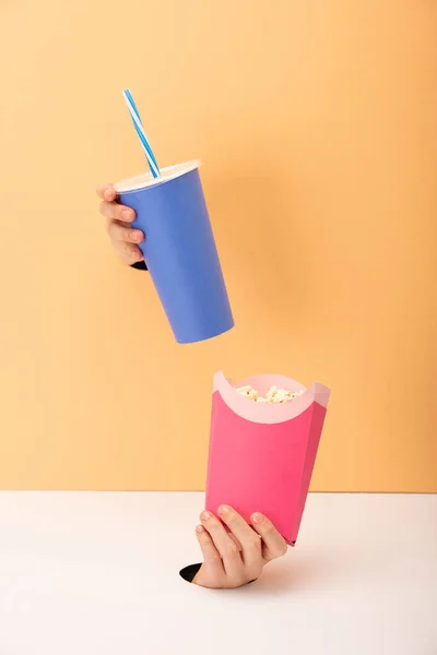 Vue recadrée des trous et femme tenant seau avec pop-corn et tasse jetable avec boisson gazeuse sur orange et blanc — Photo de stock