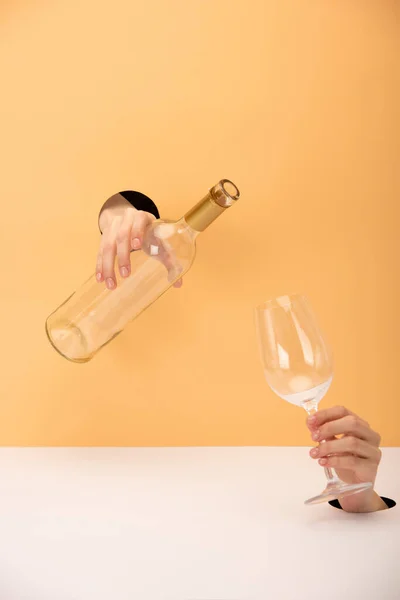 Vista recortada de la mujer sosteniendo botella y vidrio en naranja y blanco - foto de stock