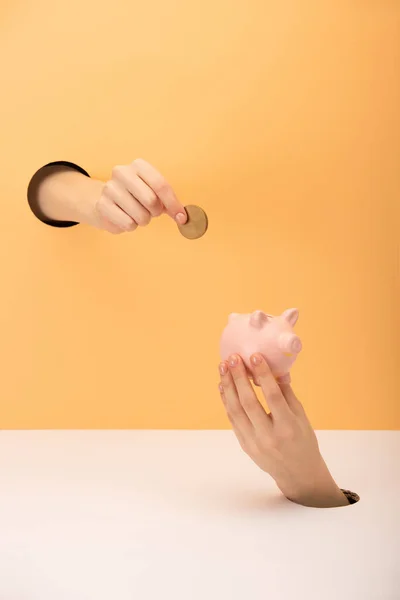 Cropped view of woman holding piggy bank and coin on orange and white — Stock Photo