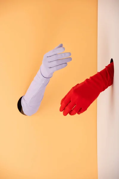 Cropped view of hands in colorful gloves on orange and white — Stock Photo