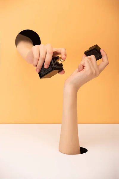 Vista cortada da mulher segurando frasco de perfume em laranja e branco — Fotografia de Stock