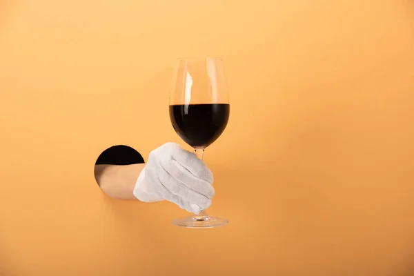 Cropped view of woman in glove holding glass of red wine on orange — Stock Photo