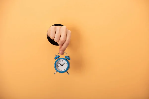 Cropped view of woman holding alarm clock on orange — Stock Photo