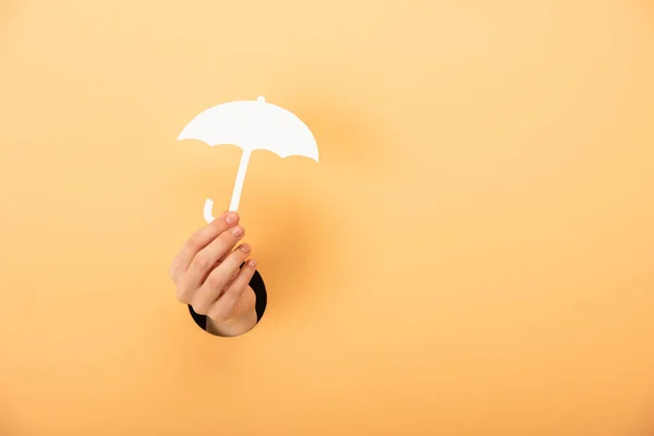 Cropped view of woman holding paper umbrella on orange — Stock Photo