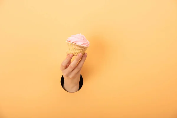 Cropped view of woman holding tasty cupcake on orange — Stock Photo