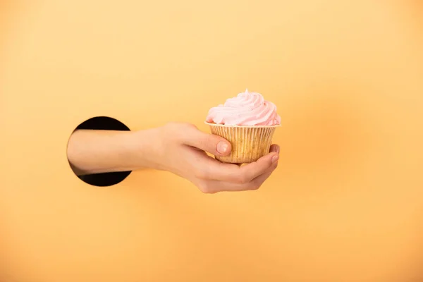 Vista cortada de mulher segurando delicioso cupcake em laranja — Fotografia de Stock