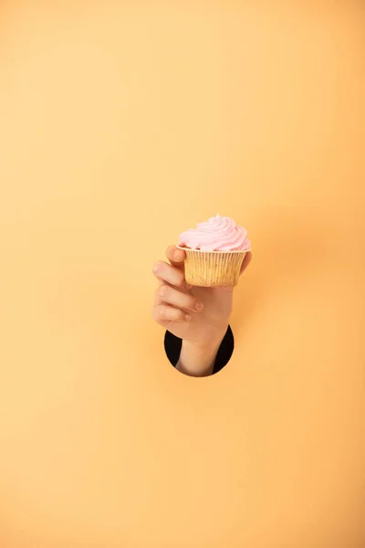 Cropped view of woman holding sweet cupcake on orange — Stock Photo