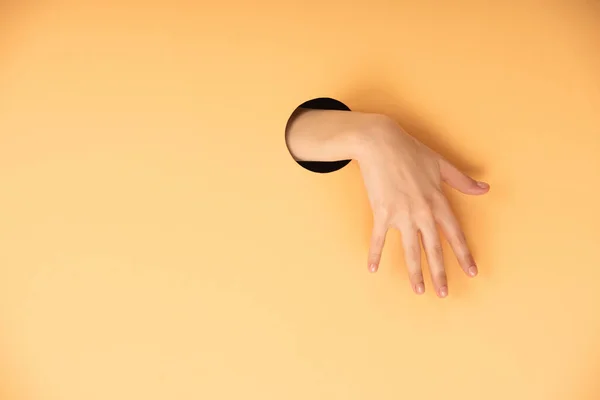 Ausgeschnittene Ansicht der Frau Hand in Hand in Loch auf orange — Stockfoto