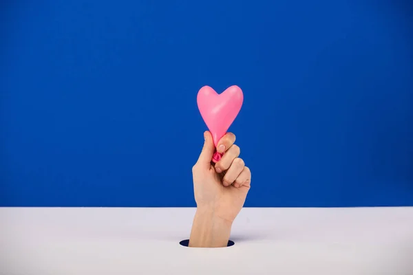 Vista recortada de la mujer sosteniendo globo rosa en forma de corazón aislado en azul - foto de stock