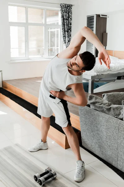 Hombre haciendo ejercicio cerca de pesas en la colchoneta de fitness en casa - foto de stock