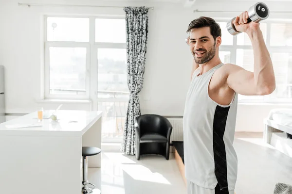 Vista lateral de um homem bonito sorrindo para a câmera enquanto treina com sinos em casa — Fotografia de Stock