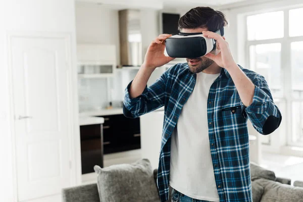 Hombre con camisa a cuadros con auriculares de realidad virtual en casa - foto de stock