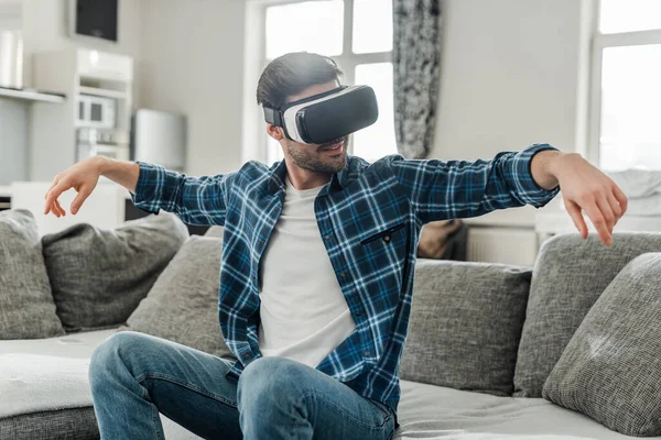 Hombre sonriente usando auriculares de realidad virtual en el sofá - foto de stock