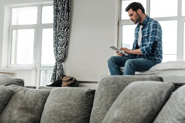 Selective focus of man in checkered shirt and jeans using digital tablet on bed at home — Stock Photo