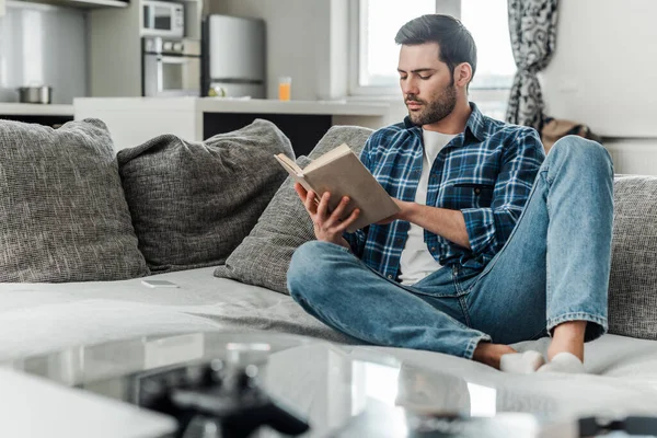 Selective focus of handsome man reading book on couch at home — Stock Photo