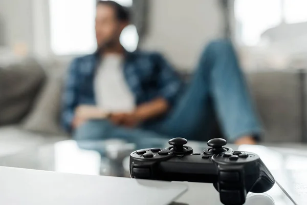 KYIV, UKRAINE - 13 AVRIL 2020 : Mise au point sélective du joystick et de l'ordinateur portable sur la table basse près de l'homme sur le canapé à la maison — Photo de stock