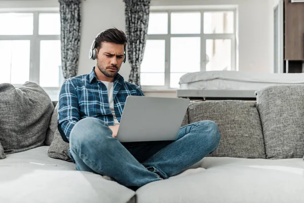 Freelancer bonito usando laptop e ouvir música em fones de ouvido no sofá — Fotografia de Stock