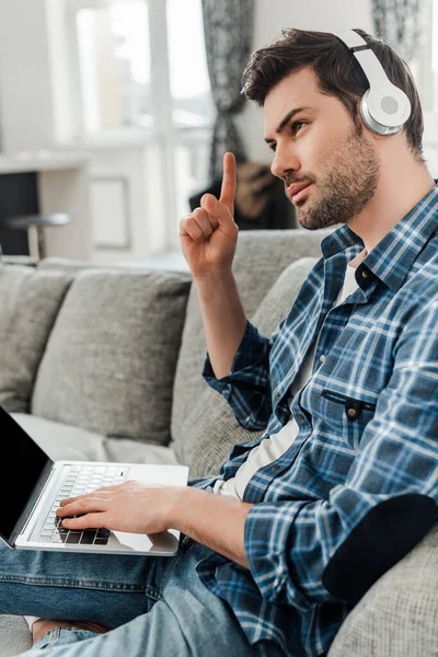 Vista lateral de belo freelancer em fones de ouvido com ideia ao usar laptop no sofá — Fotografia de Stock
