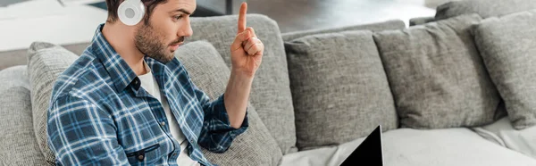 Panoramic crop of freelancer in headphones having idea while looking at laptop on sofa — Stock Photo