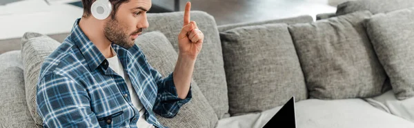 Récolte panoramique de pigiste dans les écouteurs ayant une idée tout en regardant un ordinateur portable sur le canapé — Photo de stock