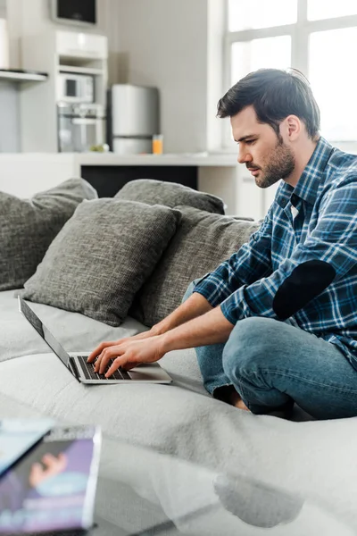 Enfoque selectivo del freelancer trabajando en el portátil en el sofá cerca de las revistas en la mesa de café — Stock Photo