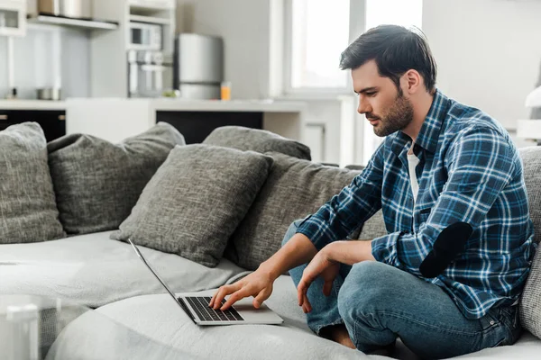 Вид сбоку на красивого человека, использующего ноутбук на диване дома — стоковое фото