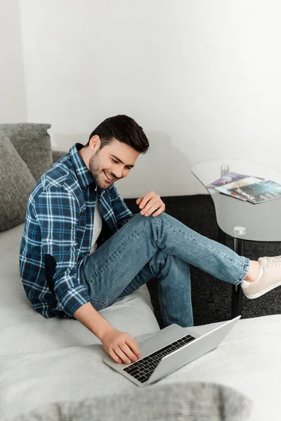 Selective focus of positive freelancer using laptop on couch in living room — Stock Photo