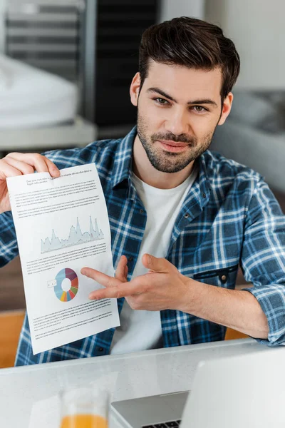 Focus selettivo di bell'uomo che punta sui grafici su carta vicino al computer portatile e al succo d'arancia — Foto stock