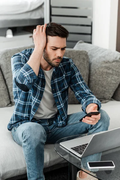Bello freelance utilizzando smartphone vicino laptop sul tavolino da caffè a casa — Foto stock
