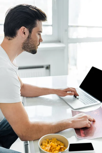 Selective focus of freelancer using laptop and document with chart near cereals on table in kitchen — Stock Photo