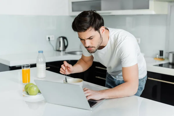 Handsome man using laptop during breakfast on table in kitchen — Stock Photo