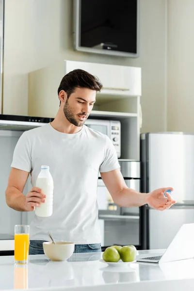 Mann hält Flasche Milch in der Küche, während er Videochat auf Laptop führt — Stockfoto