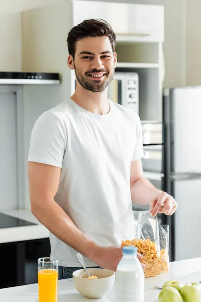 Foco seletivo de homem sorridente segurando cereais perto de suco de laranja e maçãs na mesa da cozinha — Fotografia de Stock